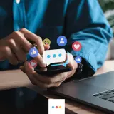 Ręce użytkownika na smartfonie, otoczone ikonami reakcji z Facebooka. Dowiedz się, jak wyróżnić post na Facebooku, by zdobyć więcej zaangażowania.