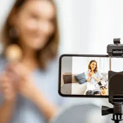 Kobieta nagrywa filmik telefonem, trzymając pędzel do makijażu.