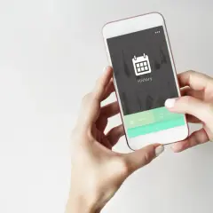 Dłonie trzymające smartfon z ikoną kalendarza i napisem "History" na ekranie.