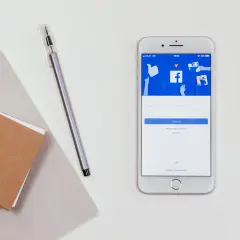 Telefon z ekranem logowania Facebooka. Obok notatnik i długopis. Jak zobaczyć hasło na Facebooku?