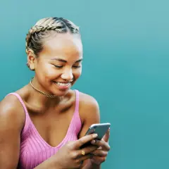 Uśmiechnięta dziewczyna z warkoczami przegląda telefon, szukając inspiracji, jak zrobić ankietę na Facebooku.