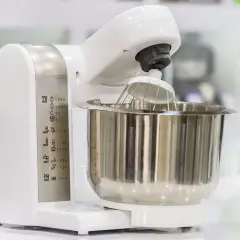 Biały robot kuchenny z metalową misą i trzepaczką. Na obudowie widoczne ikony funkcji, pomocne przy wyborze, jaki robot kuchenny wybrać blog.