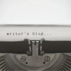 Zbliżenie na starą maszynę do pisania z tekstem "writer's blog..." na papierze.