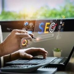 Osoba pracuje przy laptopie, analizując dane SEO. Wirtualny interfejs pokazuje ikony związane z marketingiem cyfrowym. To praca content seo manager co to jest.