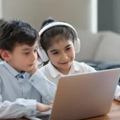 Dzieci uczą się, jak otworzyć YT w przeglądarce, korzystając z laptopa. Dziewczynka ma słuchawki.