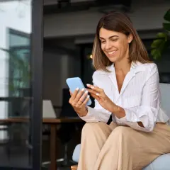 Uśmiechnięta content managerka przegląda coś na telefonie, siedząc na kanapie w nowoczesnym biurze.