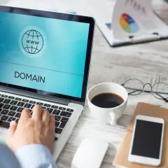 Osoba pisząca na laptopie z ikoną domeny i tekstem "DOMAIN" na ekranie.