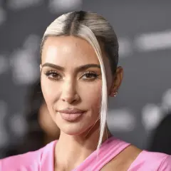 Kim Kardashian w różowej sukience, z blond pasmem włosów opadającym na twarz. Jej spojrzenie idealnie pasuje do jej stylu na Instagramie.