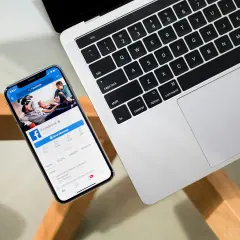 Smartfon z otwartą aplikacją Facebook obok laptopa.