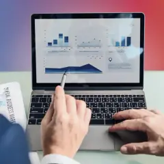 Analiza danych na laptopie. Ręka wskazuje na wykres, a obok leży dokument "Global Business Markets". To pokazuje, content co to znaczy w praktyce.