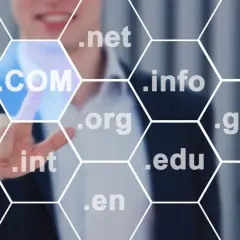 Biznesmen wybiera domenę .COM, pokazując, jak sprawdzić domenę. Widoczne są też inne rozszerzenia: .uk, .net, .info, .us, .org, .gov, .int, .edu, .en.