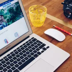 Laptop z ekranem pokazującym jak zrobić post sponsorowany na Facebooku, obok myszka, długopis i aparat.