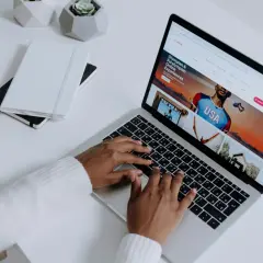 Osoba pisząca na laptopie, na ekranie którego wyświetla się strona Airbnb z ofertą "Olympian & Paralympian Online Experiences".