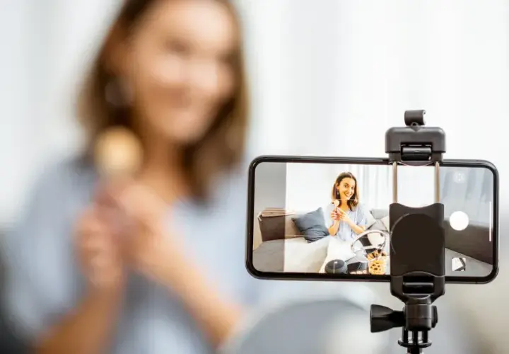 Kobieta nagrywa filmik telefonem, trzymając pędzel do makijażu.