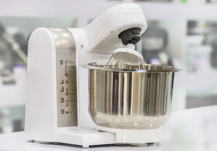 Biały robot kuchenny z metalową misą i trzepaczką. Na obudowie widoczne ikony funkcji, pomocne przy wyborze, jaki robot kuchenny wybrać blog.