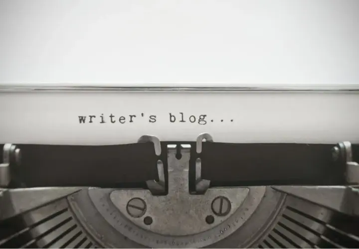 Zbliżenie na starą maszynę do pisania z tekstem "writer's blog..." na papierze.