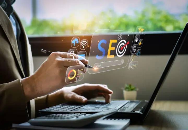 Osoba pracuje przy laptopie, analizując dane SEO. Wirtualny interfejs pokazuje ikony związane z marketingiem cyfrowym. To praca content seo manager co to jest.