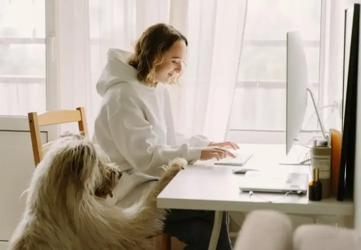 Content specialist pracuje przy komputerze, towarzyszy jej kudłaty pies.