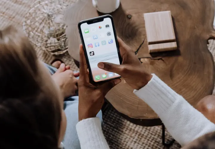 Osoba trzyma smartfon z ikonami aplikacji, w tym Facebooka. Dowiedz się, jak zablokować zdjęcia na Facebooku, aby chronić swoją prywatność.