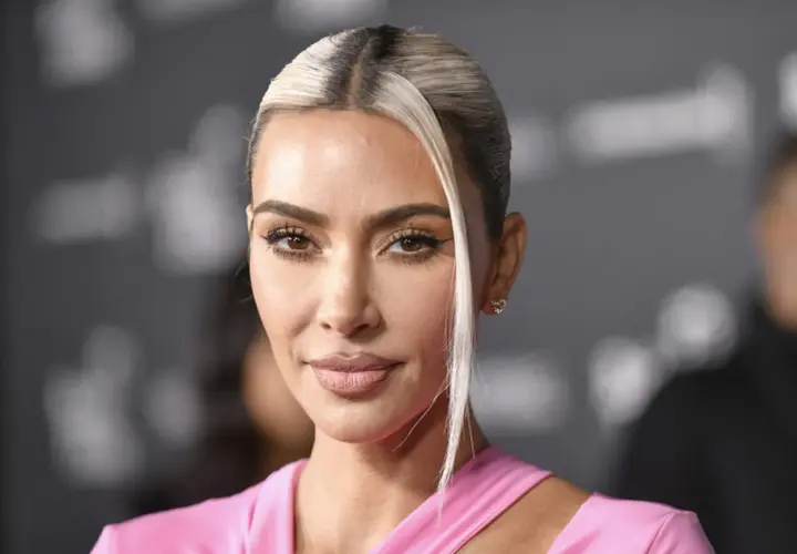 Kim Kardashian w różowej sukience, z blond pasmem włosów opadającym na twarz. Jej spojrzenie idealnie pasuje do jej stylu na Instagramie.