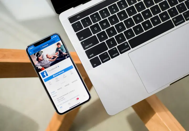 Smartfon z otwartą aplikacją Facebook obok laptopa.