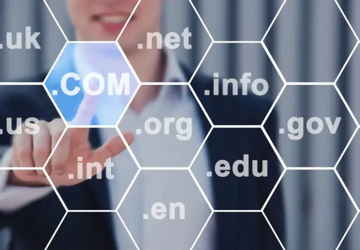 Biznesmen wybiera domenę .COM, pokazując, jak sprawdzić domenę. Widoczne są też inne rozszerzenia: .uk, .net, .info, .us, .org, .gov, .int, .edu, .en.