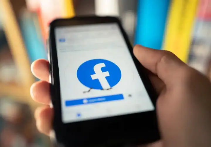 Dłoń trzyma smartfon z ekranem logowania Facebooka. Chcesz wiedzieć, jak usunąć Facebook na stałe?