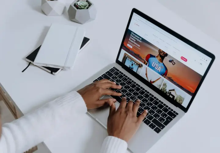 Osoba pisząca na laptopie, na ekranie którego wyświetla się strona Airbnb z ofertą "Olympian & Paralympian Online Experiences".