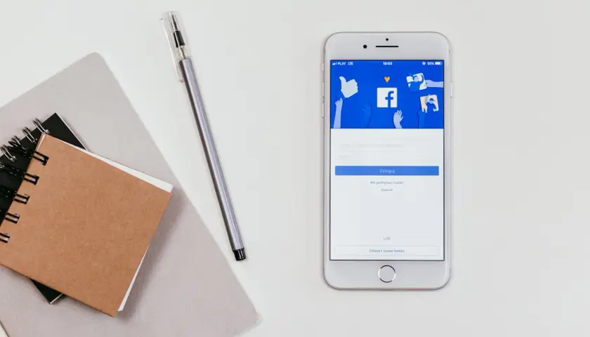 Telefon z ekranem logowania Facebooka. Obok notatnik i długopis. Jak zobaczyć hasło na Facebooku?