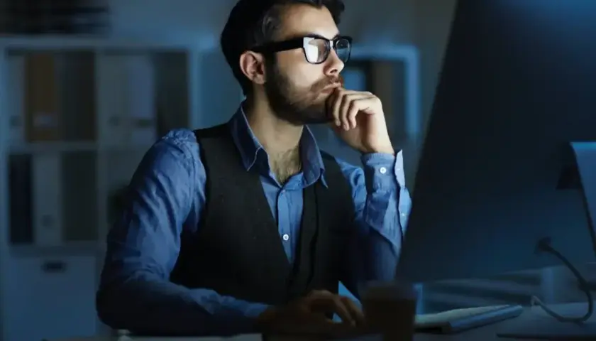 Mężczyzna w okularach pracuje przy komputerze w nocy.