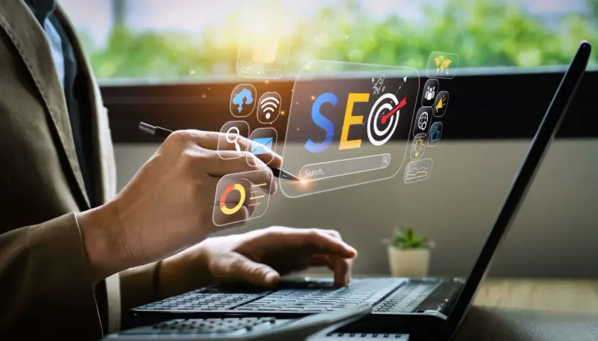 Osoba pracuje przy laptopie, analizując dane SEO. Wirtualny interfejs pokazuje ikony związane z marketingiem cyfrowym. To praca content seo manager co to jest.