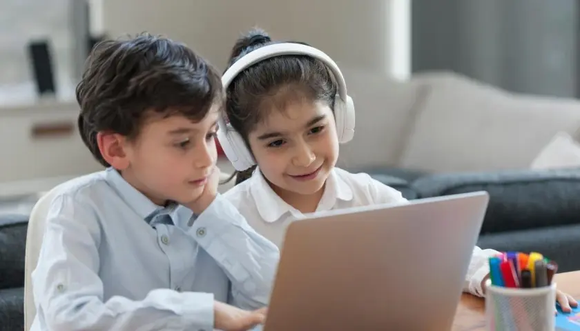 Dzieci uczą się, jak otworzyć YT w przeglądarce, korzystając z laptopa. Dziewczynka ma słuchawki.