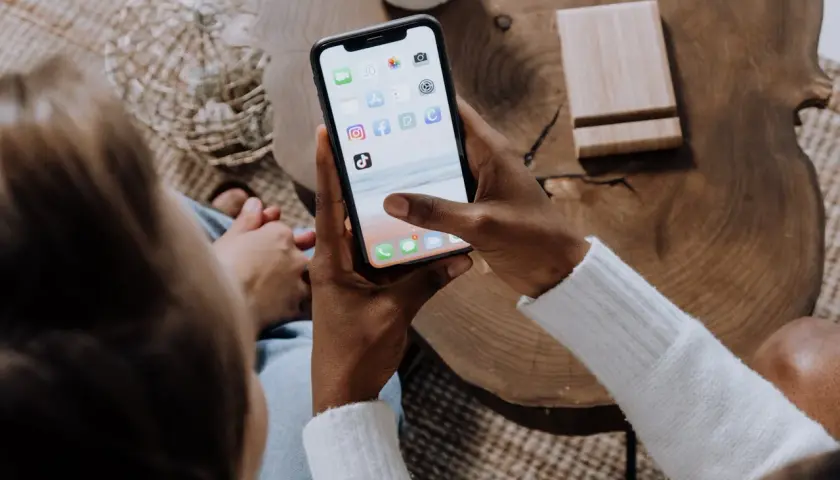 Osoba trzyma smartfon z ikonami aplikacji, w tym Facebooka. Dowiedz się, jak zablokować zdjęcia na Facebooku, aby chronić swoją prywatność.