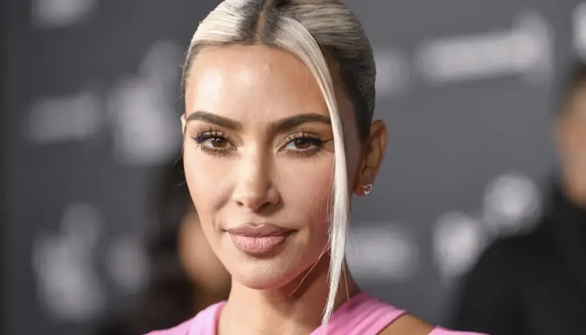 Kim Kardashian w różowej sukience, z blond pasmem włosów opadającym na twarz. Jej spojrzenie idealnie pasuje do jej stylu na Instagramie.