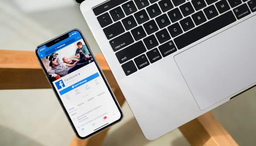 Smartfon z otwartą aplikacją Facebook obok laptopa.