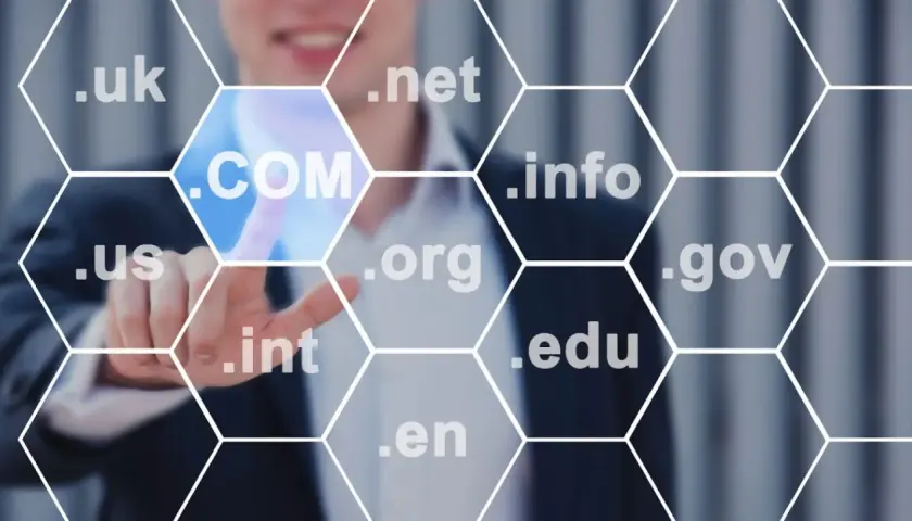Biznesmen wybiera domenę .COM, pokazując, jak sprawdzić domenę. Widoczne są też inne rozszerzenia: .uk, .net, .info, .us, .org, .gov, .int, .edu, .en.