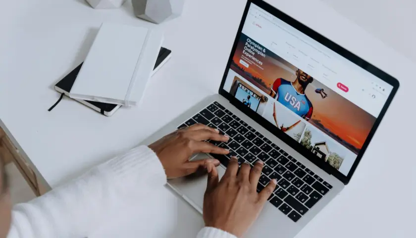 Osoba pisząca na laptopie, na ekranie którego wyświetla się strona Airbnb z ofertą "Olympian & Paralympian Online Experiences".