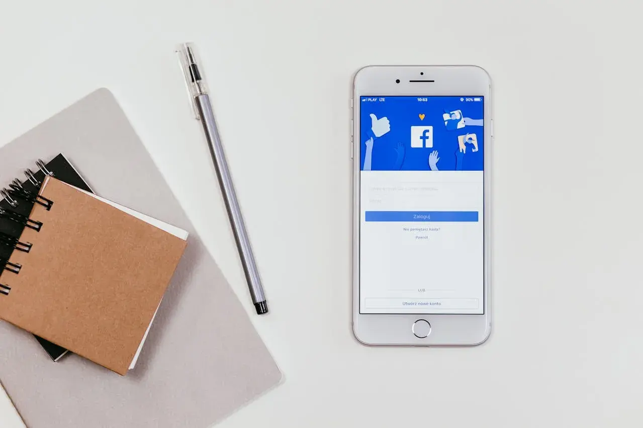 Telefon z ekranem logowania Facebooka. Obok notatnik i długopis. Jak zobaczyć hasło na Facebooku?