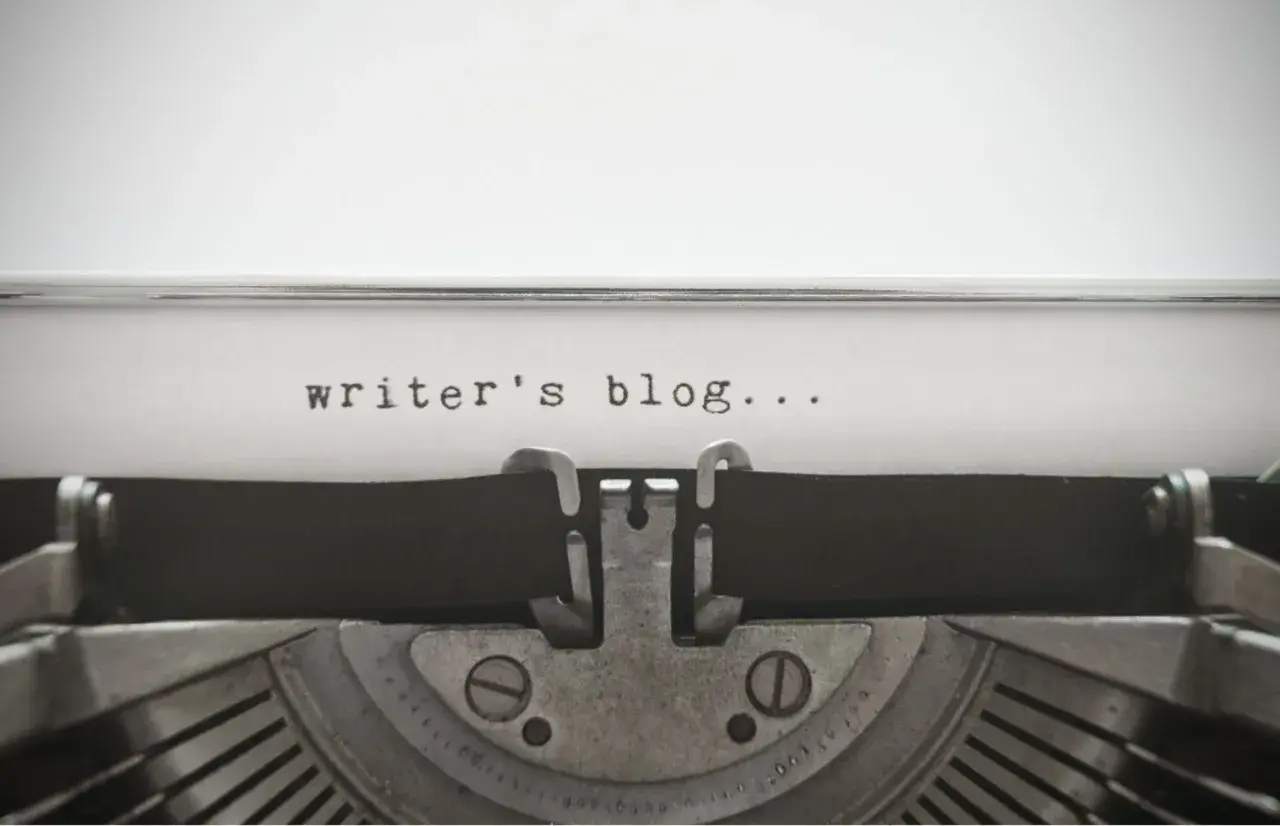 Zbliżenie na starą maszynę do pisania z tekstem "writer's blog..." na papierze.
