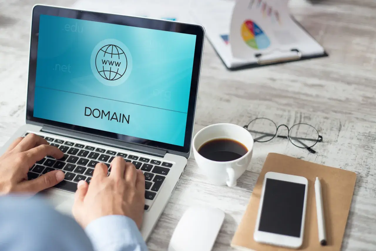 Osoba pisząca na laptopie z ikoną domeny i tekstem "DOMAIN" na ekranie.