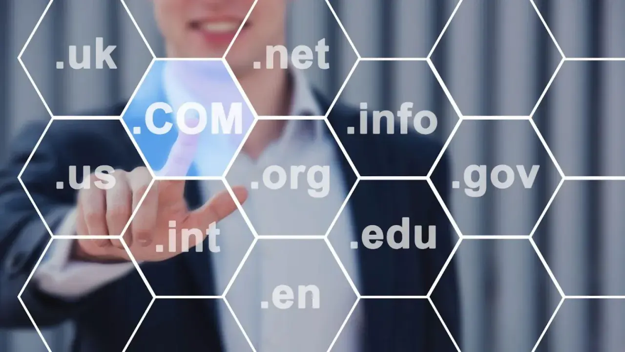 Biznesmen wybiera domenę .COM, pokazując, jak sprawdzić domenę. Widoczne są też inne rozszerzenia: .uk, .net, .info, .us, .org, .gov, .int, .edu, .en.