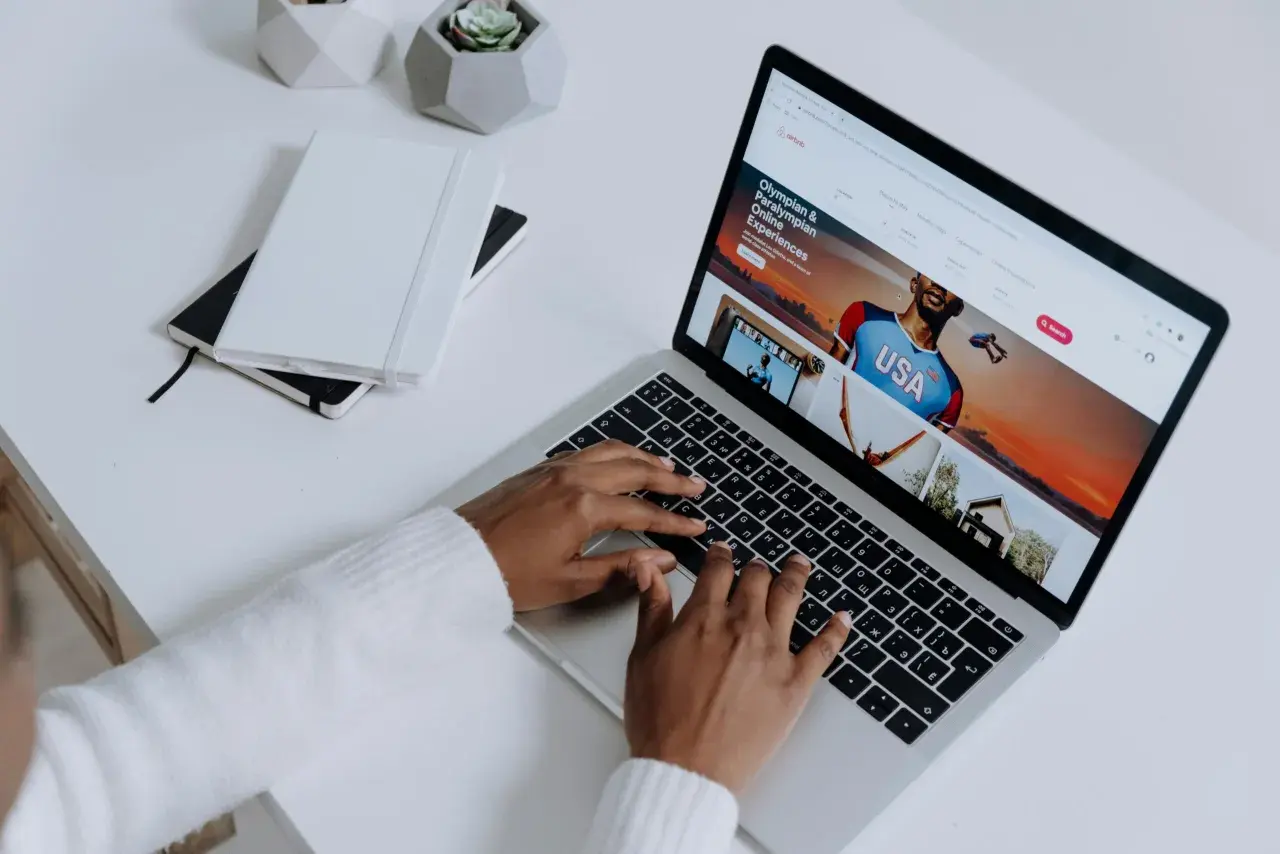 Osoba pisząca na laptopie, na ekranie którego wyświetla się strona Airbnb z ofertą "Olympian & Paralympian Online Experiences".