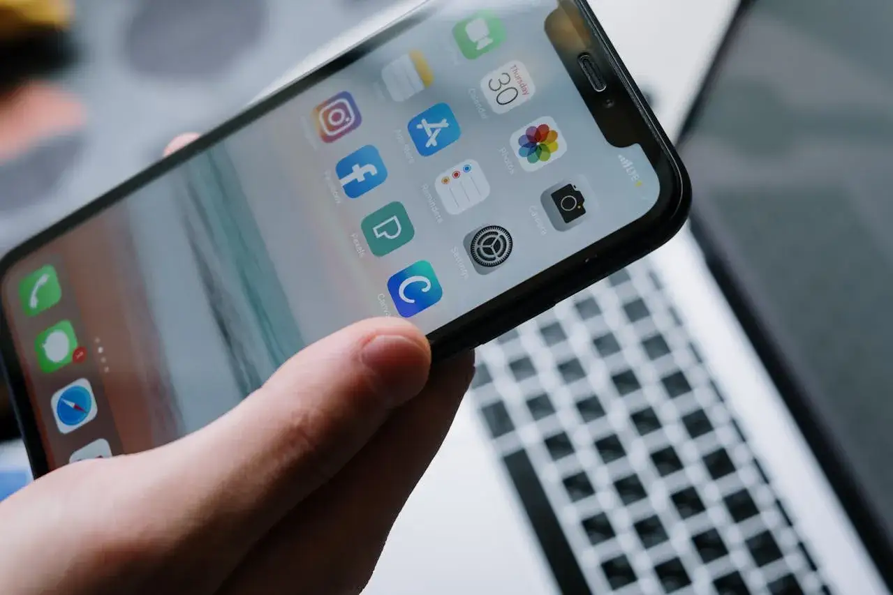 Dłoń trzyma iPhone'a z ikonami aplikacji, w tym Facebooka. Dowiedz się, jak zmienić avatar na Facebooku.