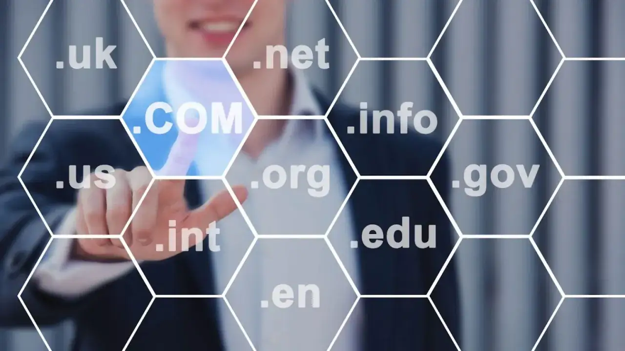 Biznesmen wybiera .COM, zastanawiając się, gdzie kupić domenę. Widoczne inne rozszerzenia: .uk, .net, .info, .us, .org, .gov, .int, .edu, .en.